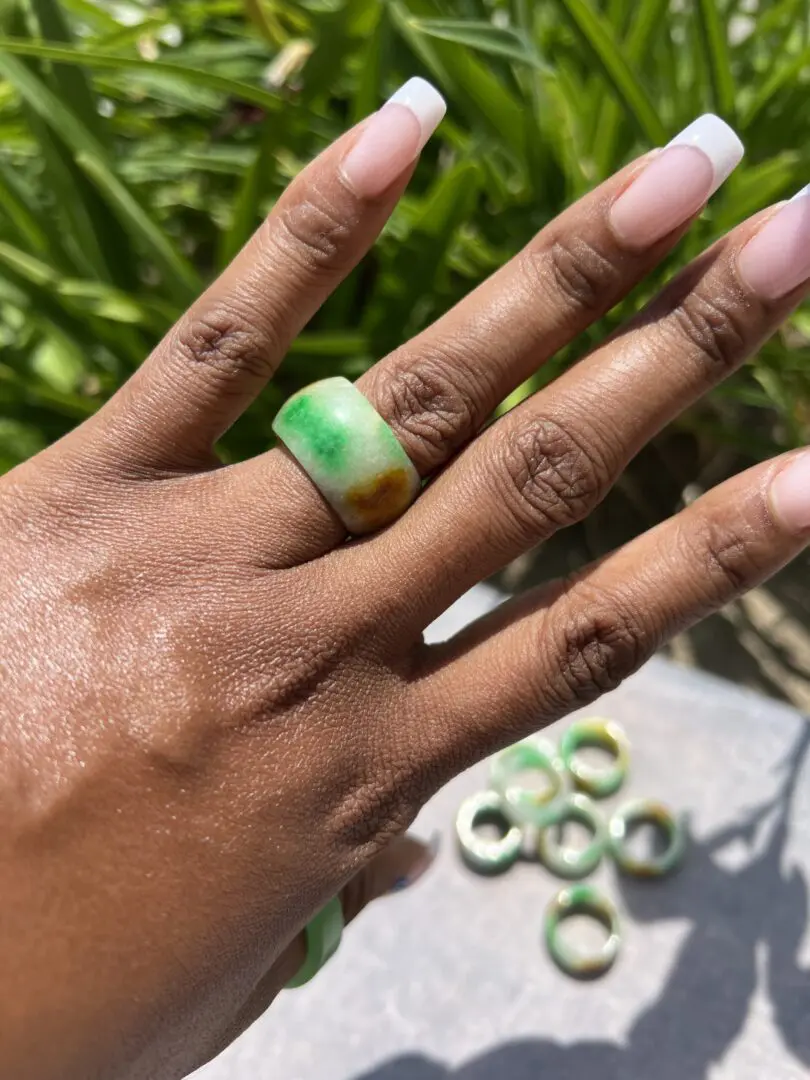 A woman 's hand with a green and white ring on her finger. A woman 's hand with a green and white ring on her finger.