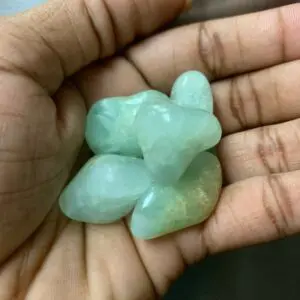 Hand holding green gemstone tumbles.