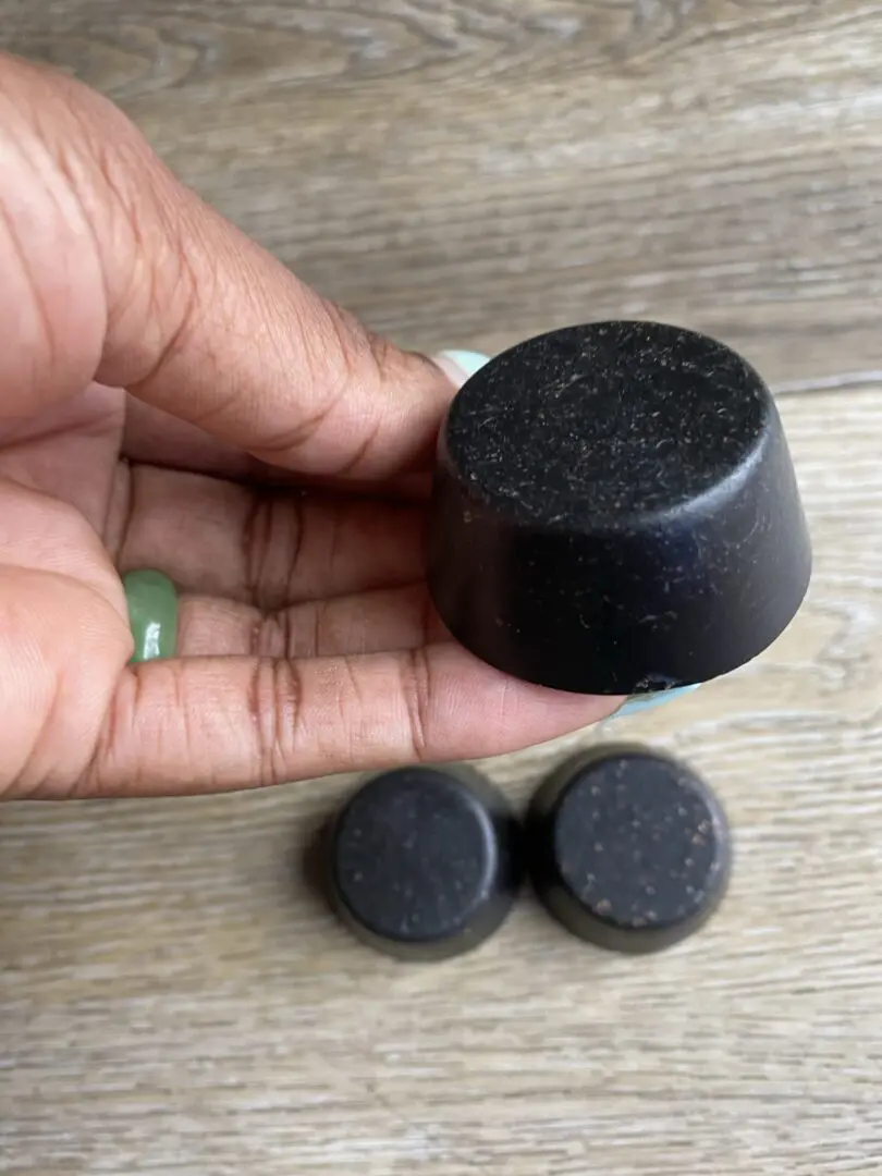 Hand holding a black round soap bar. Hand holding a black round soap bar.
