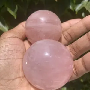 Two pink rose quartz spheres in hand.