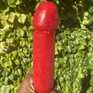 A bright red chili pepper held against a green leafy background.