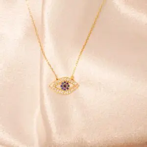 Gold evil eye necklace on pink fabric.