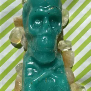 A green skull candle with yellow stones around it.