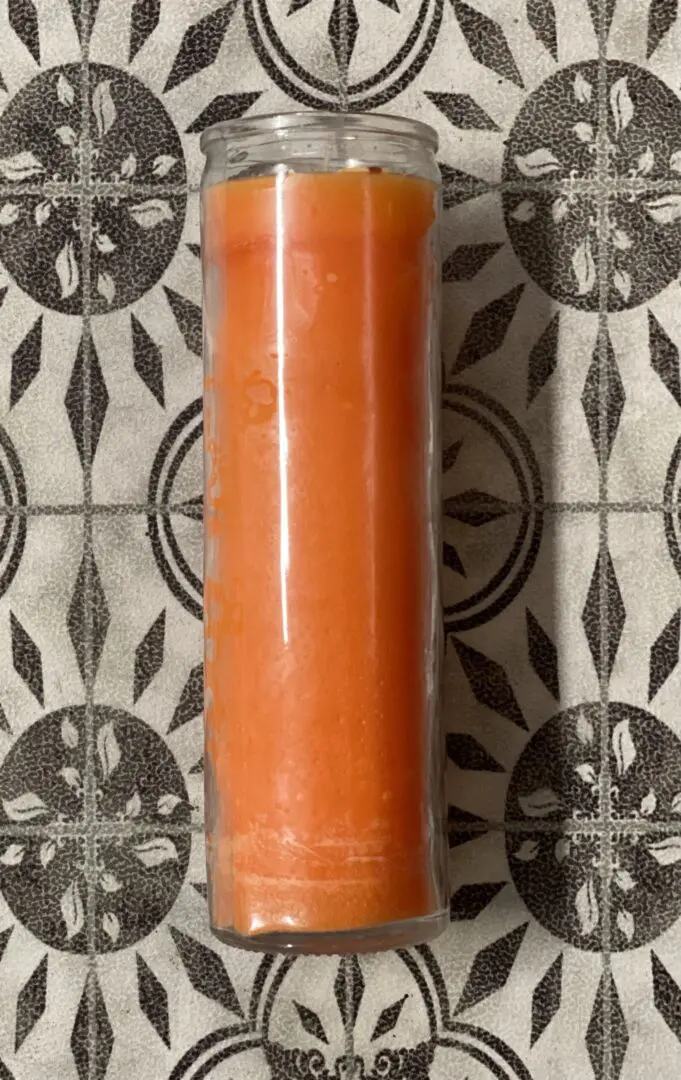 A candle is sitting on the floor of a tiled wall. A candle is sitting on the floor of a tiled wall.