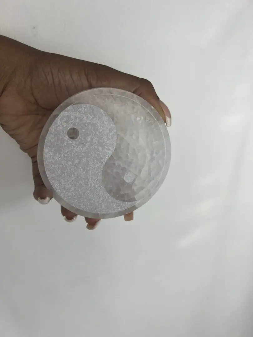 A person holding a glass dish with an image of yin yang. A person holding a glass dish with an image of yin yang.