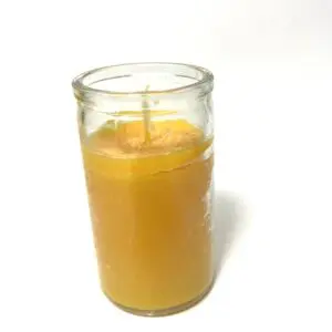 A candle in a glass is lit and has an orange.