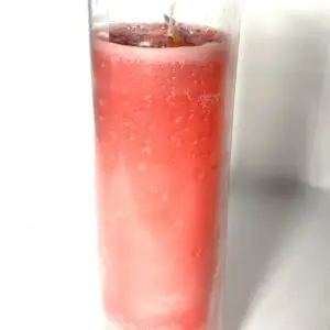 A glass of pink liquid with ice in it.
