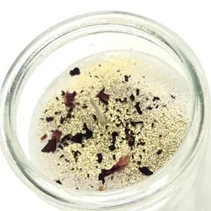 A glass jar containing a clear liquid with floating herbs and spices.