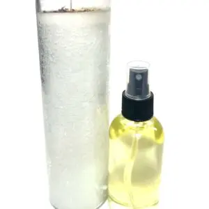 A spray bottle of yellow liquid next to a roll of white cotton pads.