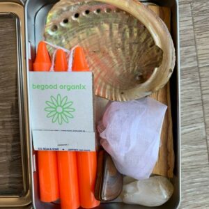 Orange candles, seashell, and white cloth in tin.