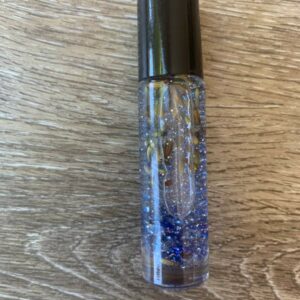 Glass roller bottle with blue glitter and herbs.