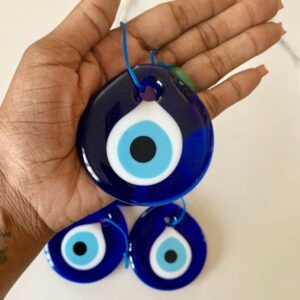 Three blue evil eye charms in hand.