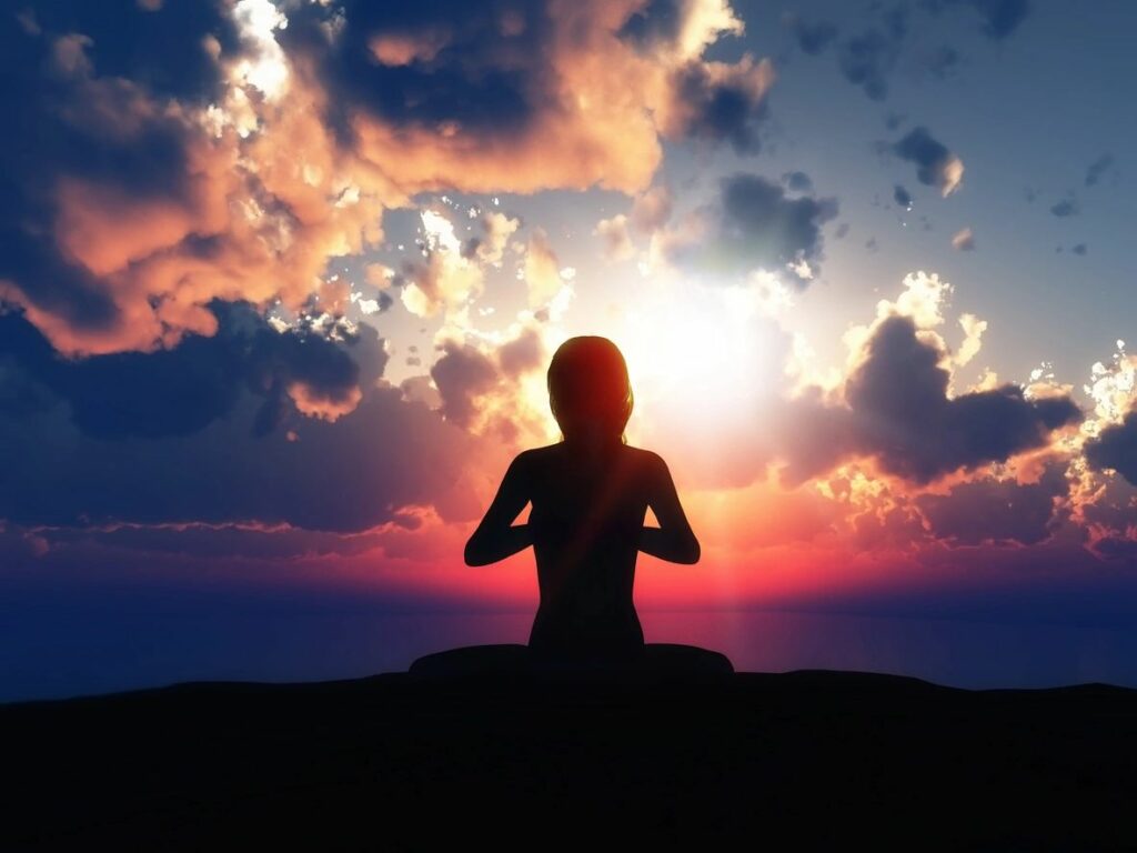 Silhouette of woman meditating at sunset.