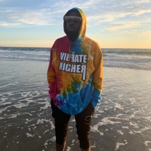 Man in tie-dye hoodie on the beach.