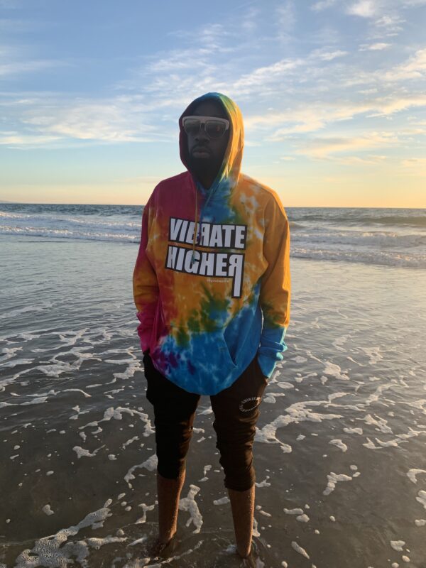 Man in tie-dye hoodie on the beach.