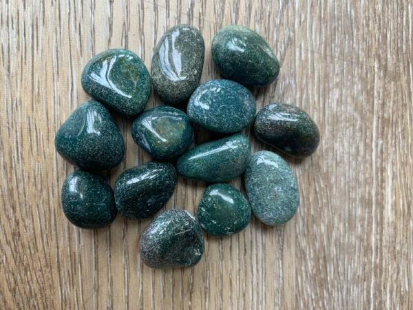 Green moss agate tumbled stones on wood.