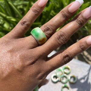 A woman 's hand with a green and white ring on her finger.