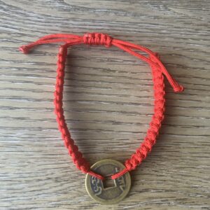 Red string bracelet with a coin charm.