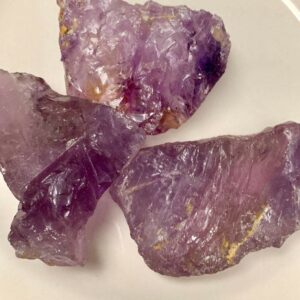 Three rough amethyst crystals on a plate.