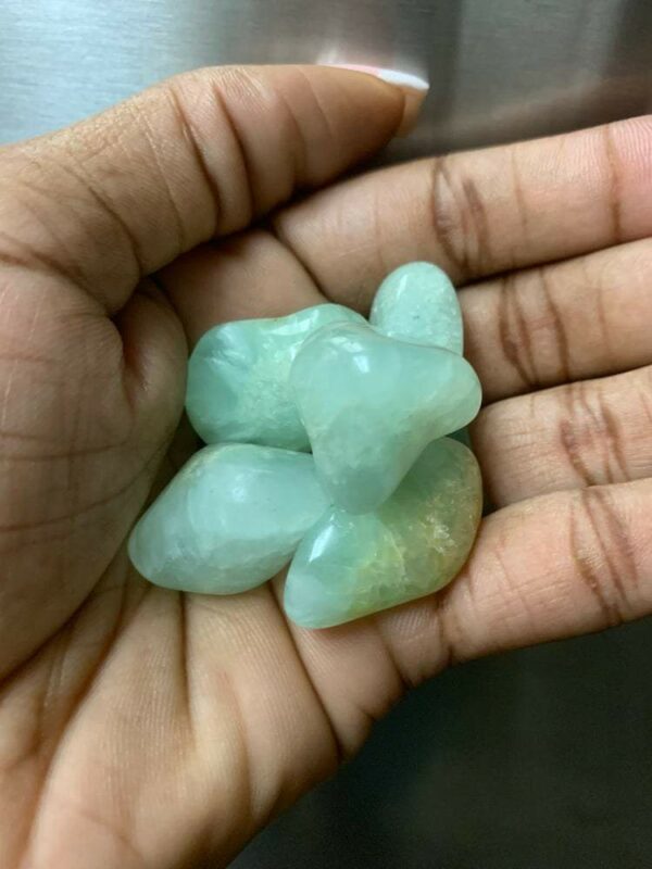 Hand holding green gemstone tumbles.