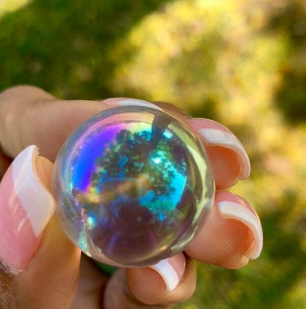 A hand holding a clear iridescent sphere.