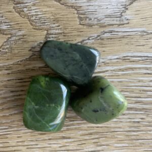 Three green jade stones on wood.