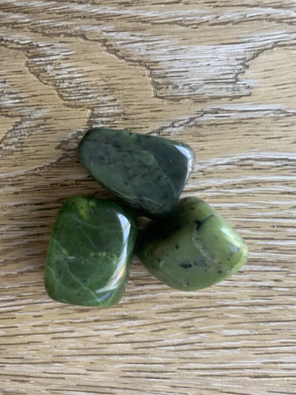 Three green jade stones on wood.