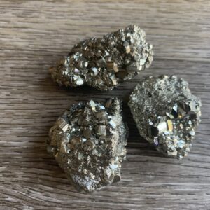 Three pyrite crystals on wood background.