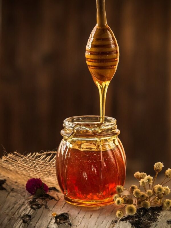 Honey dripping into a glass jar.