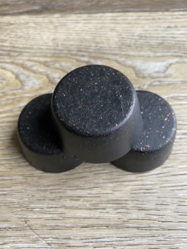 Three round black soap bars on wood.