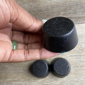 Hand holding a black round soap bar.