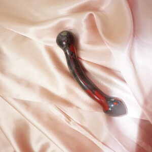 Red and black glass dildo on satin sheet.