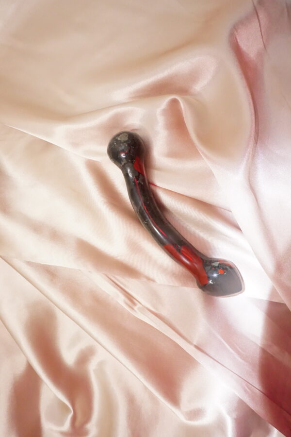 Red and black glass dildo on satin sheet.