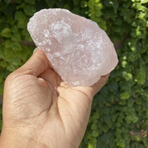 Hand holding a pink rose quartz crystal.