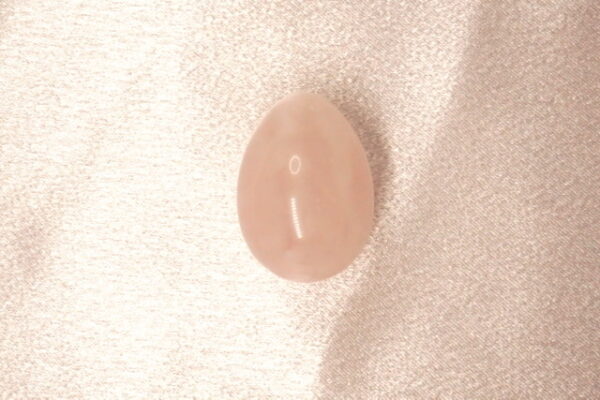 Pink oval gemstone on white fabric.