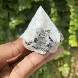 White crystal with black inclusions in hand.