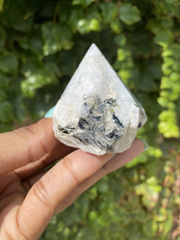 White crystal with black inclusions in hand.