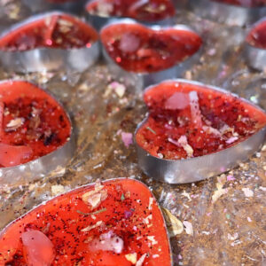 Red heart-shaped candles with glitter and petals.