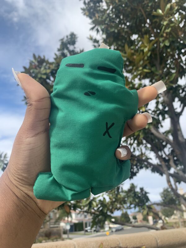 Green hand-sewn plush toy with an X.