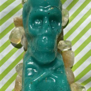 A green skull candle with yellow stones around it.