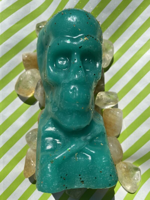 A green skull candle with yellow stones around it.