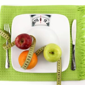 A plate with an apple, orange and measuring tape on it.