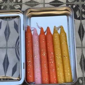 A tin of candles with different colors in them.