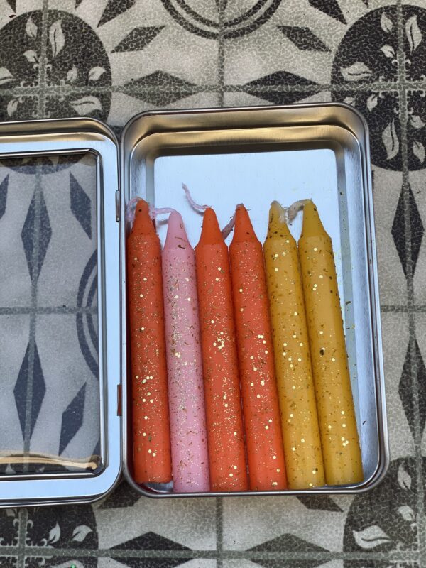 A tin of candles with different colors in them.