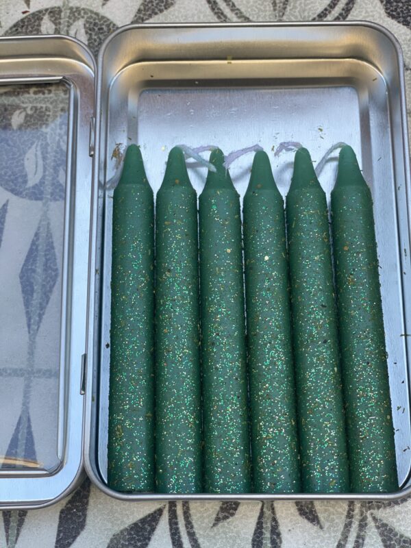 A box of green candles with the wax being burned.