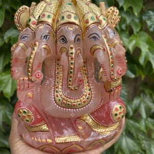 A hand holding an elephant statue in front of some bushes.