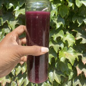 A person holding a glass of juice in front of some leaves.