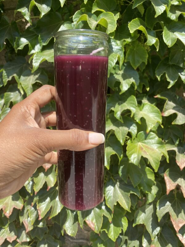 A person holding a glass of juice in front of some leaves.