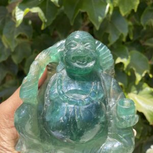 A person holding a green buddha statue in front of some bushes.