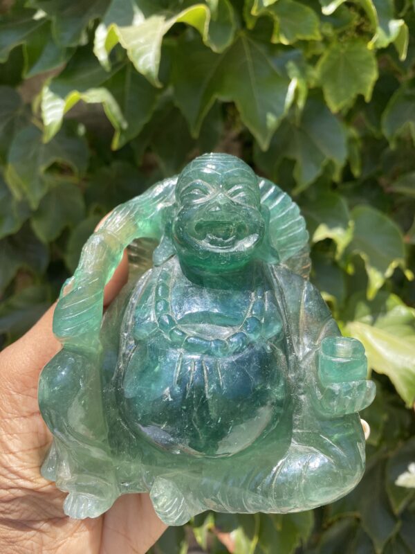 A person holding a green buddha statue in front of some bushes.